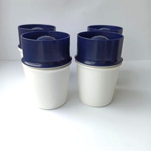 Può includere: Quattro tazze bianche con coperchi blu. Le tazze sono impilate l'una sull'altra.