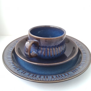 May include: A blue and brown ceramic teacup and saucer set with a geometric pattern. The saucer has a raised edge and the cup has a textured design.
