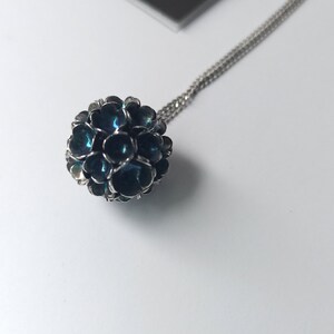 Pode incluir: Um colar de corrente de prata com um pingente azul e prateado. O pingente &eacute; uma esfera feita de muitas pequenas flores sobrepostas.
