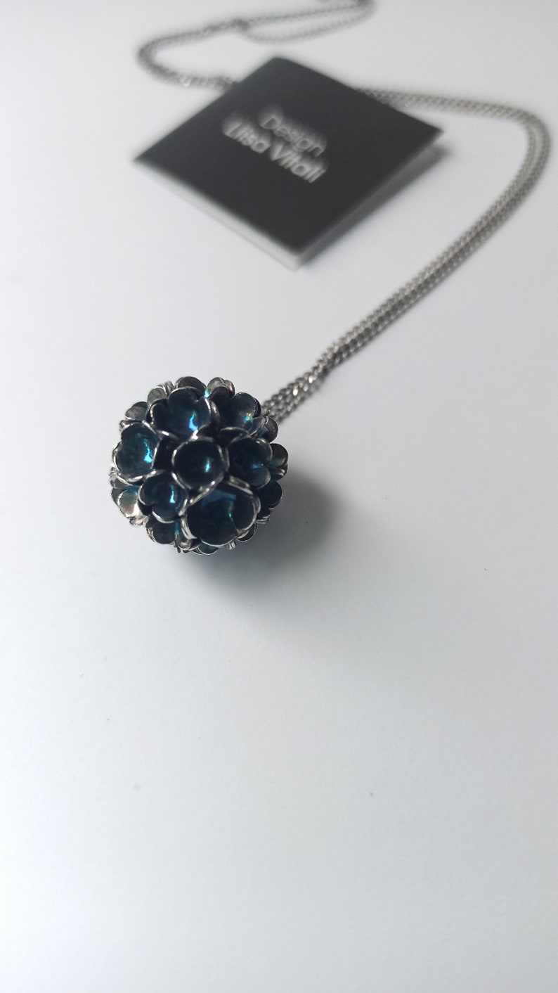 Pode incluir: Um colar de corrente de prata com um pingente azul e prateado. O pingente &eacute; uma esfera feita de muitas pequenas flores sobrepostas.