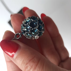 Pode incluir: Um colar de corrente de prata com um pingente esf&eacute;rico azul e prateado. A esfera &eacute; feita de muitas pedras pequenas e facetadas.