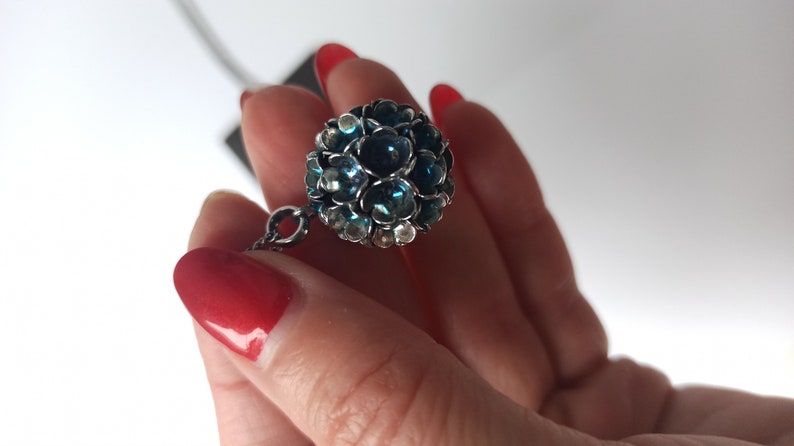 Pode incluir: Um colar de corrente de prata com um pingente esf&eacute;rico azul e prateado. A esfera &eacute; feita de muitas pedras pequenas e facetadas.