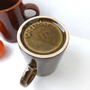 Puede incluir: Una taza de cer&aacute;mica marr&oacute;n con asa. La base de la taza tiene un esmalte verde con las palabras "W. Germany" y el n&uacute;mero "026" impresos en ella.