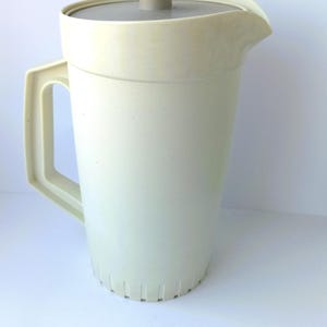 May include: Off-white plastic jug with a matching lid and handle. The jug has a textured surface and a spout for easy pouring. The lid is grey with a beige knob. A classic kitchenware item.