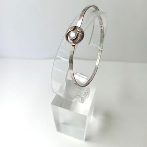 May include: A silver bangle bracelet with a small, clear gemstone set in a circular design.