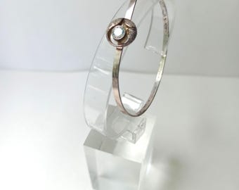 May include: A silver bangle bracelet with a small, clear gemstone set in a circular design.