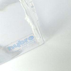 May include: A clear glass object with a label that reads "nybro SWEDEN design: paul isling". The object has a slightly textured surface and is partially visible against a white background.