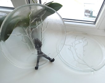 May include: Two clear glass plates with a raised design of a tree branch. The plates are on a white surface.
