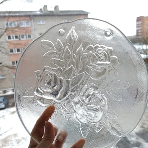 Peut inclure: Une assiette en verre transparent avec un motif en relief de roses et de feuilles. L'assiette a deux trous sur le bord supérieur.