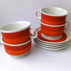 Könnte beinhalten: Set aus Vintage-Tassen und Untertassen. Die Tassen haben eine weiße Innenseite und sind mit horizontalen Bändern in Orange und Rot verziert. Die Untertassen sind weiß mit einem orangefarbenen Rand. Das Set enthält sechs Untertassen und vier Tassen.