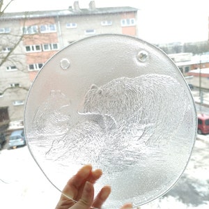 Peut inclure: Une assiette en verre transparent avec un motif en relief de deux ours polaires dans un paysage enneigé. L'assiette est ronde et a une surface légèrement texturée.