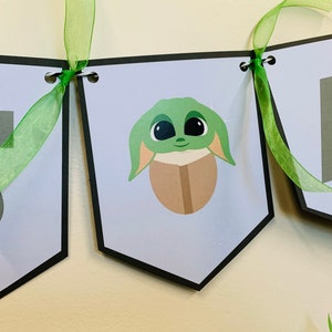 May include: A green, white, and brown banner with the word "One" and a cartoon image of a green alien character. The banner is decorated with green ribbon.