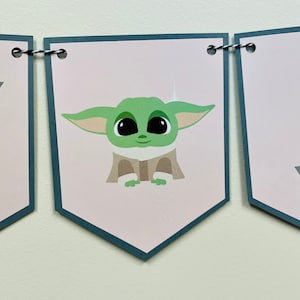 May include: A pink and gray banner with the word "Happy" and a cartoon image of a green alien character. The banner is strung with black and white twine.