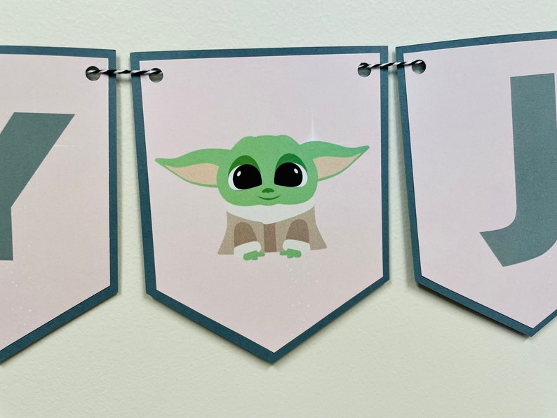 May include: A pink and gray banner with the word "Happy" and a cartoon image of a green alien character. The banner is strung with black and white twine.