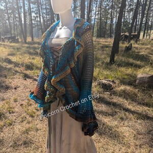 May include: A crocheted shawl with a ruffled edge in shades of teal, brown, and green. The shawl is draped over a white mannequin in a forest setting. The text "Unicorn Crochet on Etsy" is visible in the lower right corner of the image.