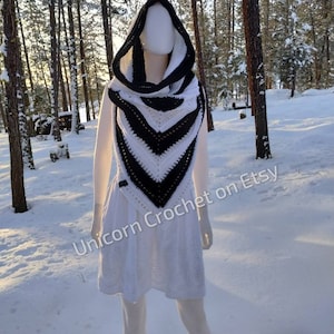 May include: Black and white hooded crochet scarf with a chevron pattern. The scarf is worn by a mannequin in a snowy forest setting. The text "Unicorn Crochet on Etsy" is visible in the lower right corner of the image.