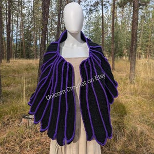 Könnte beinhalten: Ein schwarzes und violettes Häkeltuch mit einem gewellten Rand. Das Tuch ist über eine weiße Schaufensterpuppe gelegt. Der Text "Unicorn Crochet on Etsy" ist auf dem Tuch sichtbar.