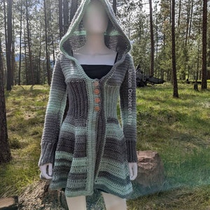 May include: A hooded crochet cardigan with a long, flowing design. The cardigan is made in a combination of grey and green yarn, with a button closure at the front. The cardigan has a large hood and pockets on the front.