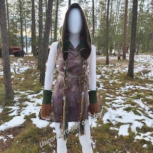 May include: A mannequin wearing a hooded dress with matching arm warmers. The dress is a tie-dye pattern in shades of brown and purple. The hood and arm warmers are green and brown. The outfit has braided accents with beads and tassels. The text "UnicornCrochet on Etsy" is visible.