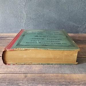 A vintage green hardcover book titled "The International Postage Stamps Junior Edition Fully Illustrated Scott Stamp & Coin Co. New York"