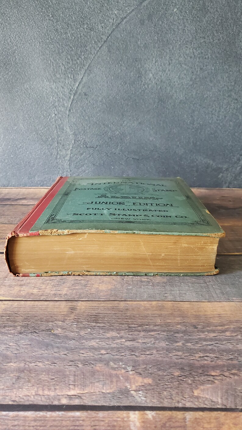 A vintage green hardcover book titled "The International Postage Stamps Junior Edition Fully Illustrated Scott Stamp & Coin Co. New York"