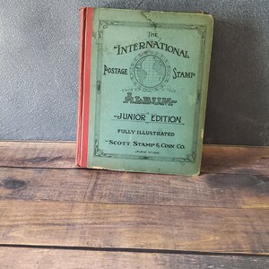 The International Postage Stamp Album Junior Edition, a green book with a globe illustration and the text "THE INTERNATIONAL POSTAGE STAMP ALBUM - JUNIOR EDITION - FULLY ILLUSTRATED - SCOTT STAMP & COIN CO. - NEW YORK"