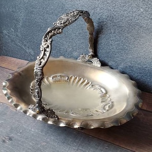 May include: A silver serving tray with an ornate handle and a scalloped edge. The tray has a decorative design on the bottom.