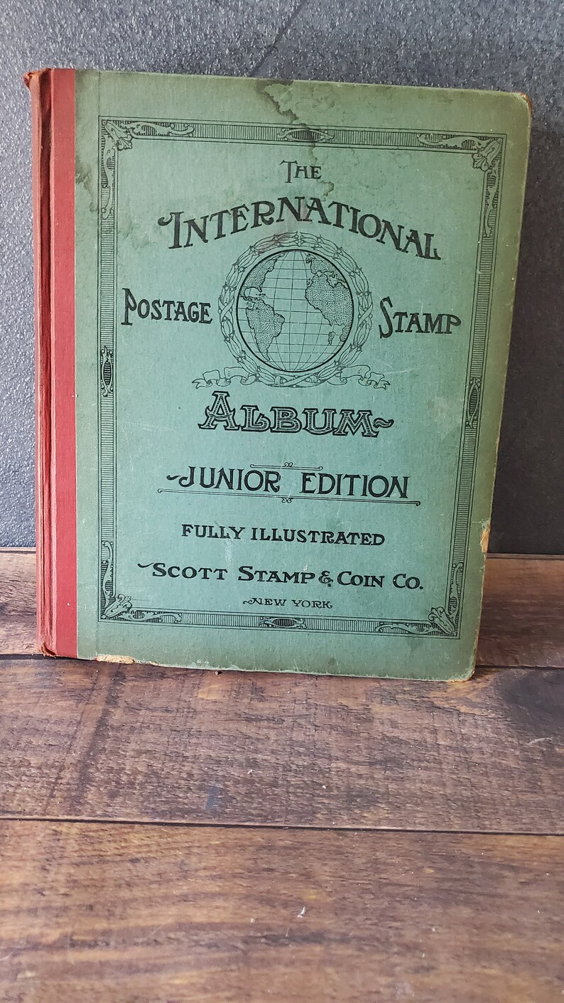 The International Postage Stamp Album Junior Edition, a green book with a globe illustration and the title in gold lettering. It is fully illustrated and published by Scott Stamp & Coin Co. in New York.