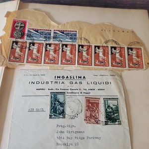 An envelope with a handwritten address to John Sirignano in Brooklyn, New York. The envelope has several stamps, including a large stamp with a picture of a woman in a blue dress and a smaller stamp with a picture of a man in a red shirt. The envelope also has the words "AIR MAIL" printed on it.