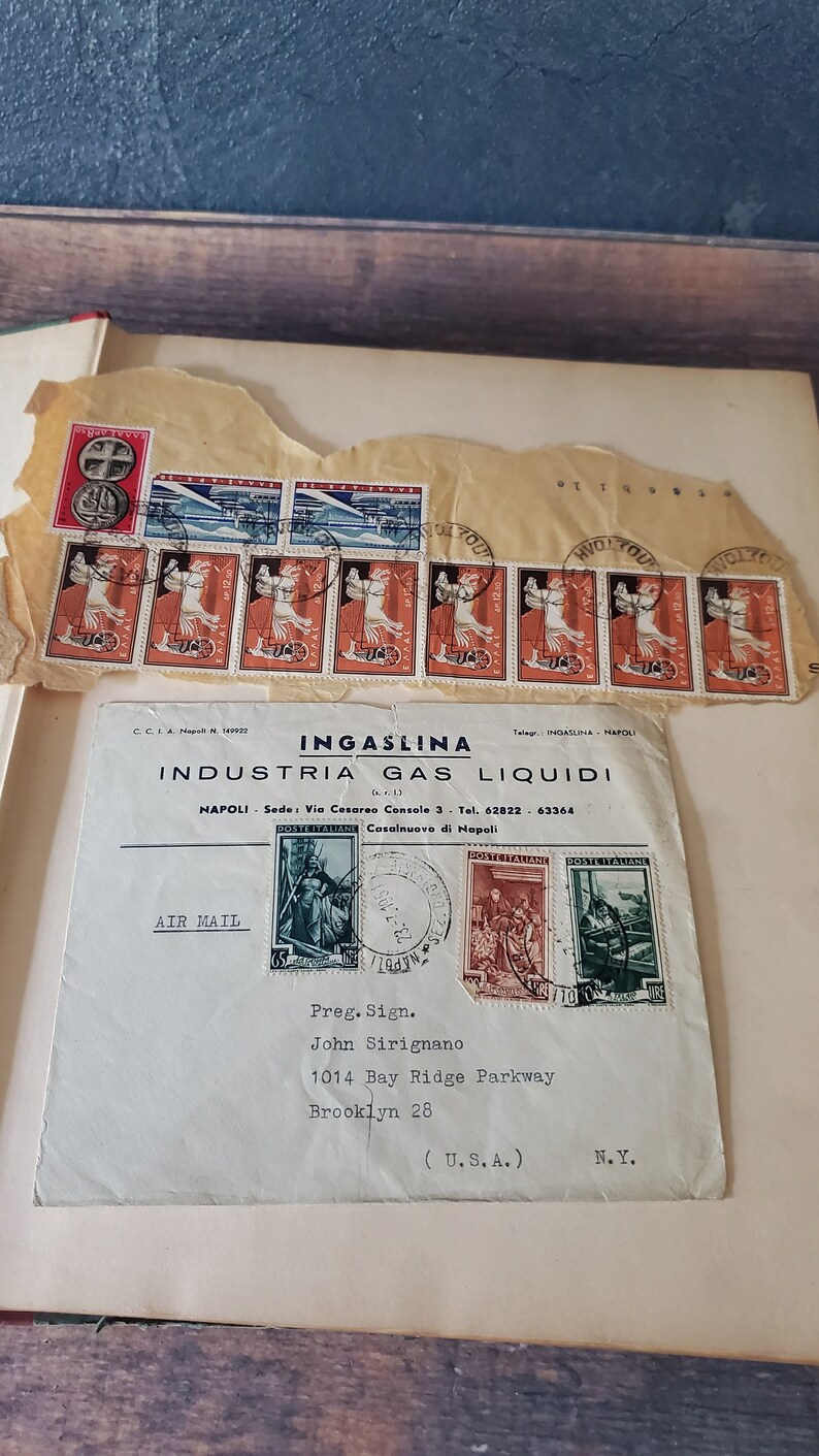 An envelope with a handwritten address to John Sirignano in Brooklyn, New York. The envelope has several stamps, including a large stamp with a picture of a woman in a blue dress and a smaller stamp with a picture of a man in a red shirt. The envelope also has the words "AIR MAIL" printed on it.