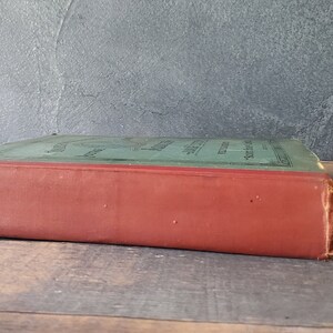 A green antique hardcover book with a red spine and black lettering. some wear to the spine of the antique stamp book