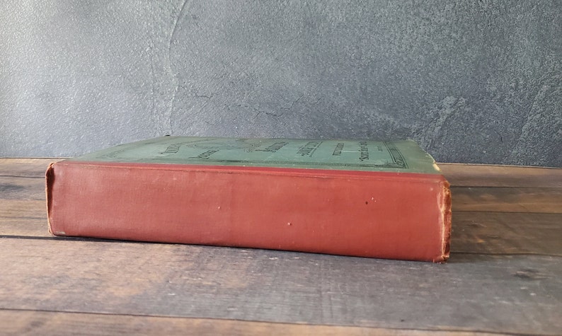 A green antique hardcover book with a red spine and black lettering. some wear to the spine of the antique stamp book