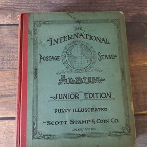 The International Postage Stamp Album Junior Edition, a green book with a globe illustration and the text "FULLY ILLUSTRATED" and "SCOTT STAMP & COIN CO. NEW YORK".