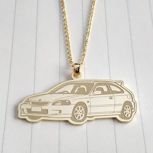 May include: A gold-coloured necklace with a pendant shaped like a car. The pendant is a detailed outline of a hatchback car, suspended from a delicate gold chain. The car pendant is approximately 3.8 cm long.