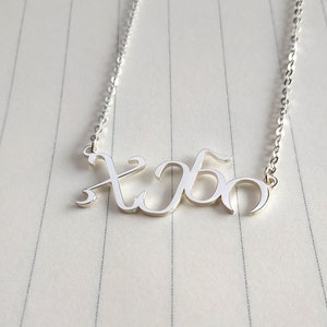 Op de afbeelding: Een zilveren ketting met een hanger in de vorm van een naam in cursief schrift die "xoxo" zegt.