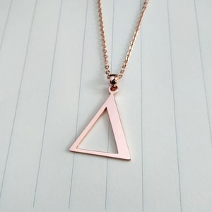Könnte beinhalten: Eine Halskette aus Roségold mit einem Dreiecksanhänger. Der Anhänger ist hohl und hat ein schlichtes Design.