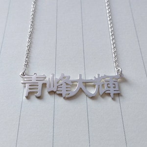Op de afbeelding: Een zilveren ketting met een hanger met de Chinese karakters "青峰大雄".
