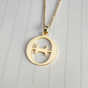 May include: A gold necklace with a pendant shaped like the letter 'O' with a smaller 'H' cut out inside.