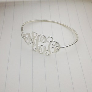 Puede incluir: Un brazalete de plata con un diseño de monograma con las letras "N C G".