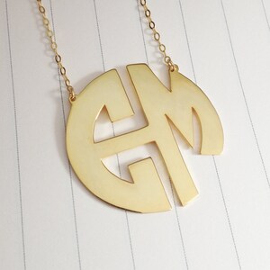 May include: Gold necklace with a large, round pendant featuring the letters "EM" in a monogram style.