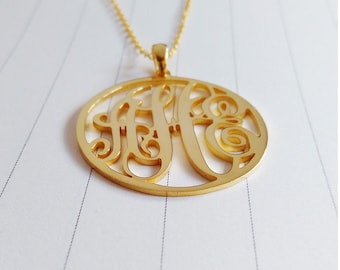 Puede incluir: Collar de oro con un colgante redondo con un diseño de monograma. El colgante está hecho de un metal delicado y calado.