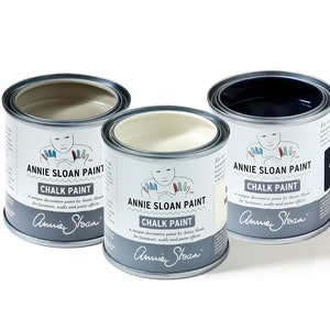 May include: Three tins of Annie Sloan Chalk Paint in the colours Old White, Graphite, and French Linen. The tins are labelled with the Annie Sloan logo and the words "Chalk Paint" and "Annie Sloan".