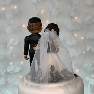 May include: A wedding cake topper featuring a black groom and a bride wearing a white dress with black lace and a white veil.