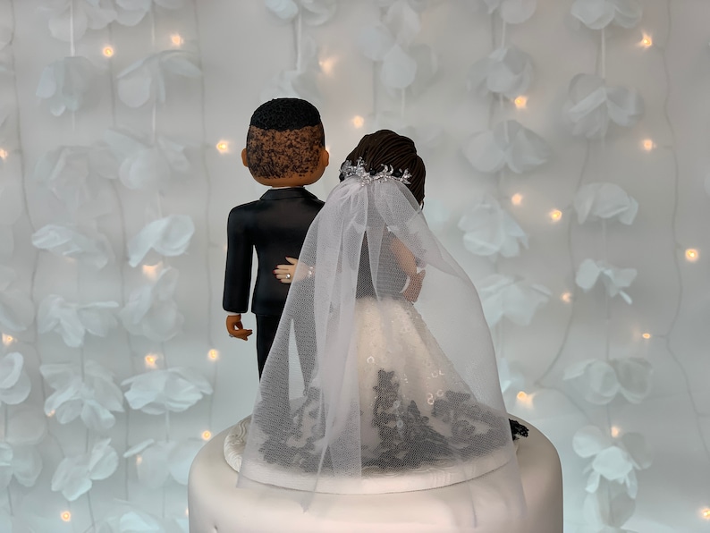 May include: A wedding cake topper featuring a black groom and a bride wearing a white dress with black lace and a white veil.
