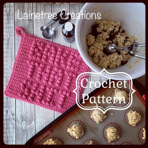 Könnte beinhalten: Ein rosa Häkel-Topflappen mit einem strukturierten Noppenmuster. Der Topflappen liegt auf einer Holzoberfläche mit dem Text "LaineTree Creations" und "Crochet Pattern" in Weiß.