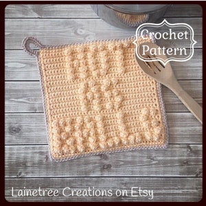 May include: A crocheted pot holder with a textured design in a light peach colour. The pot holder has a loop handle and a grey border. The text "Crochet Pattern" is visible in the image.