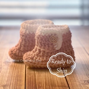 May include: A pair of pink and white crocheted baby booties with a wooden button that says "Handmade with love".