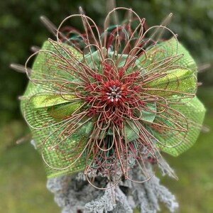 May include: A green and red wire mesh bow with a sparkly center. The bow is tied with a red ribbon and has a wire loop for hanging.