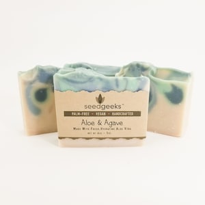 May include: Four bars of handmade soap with a light beige base and swirled blue and green tops. The bars are labeled "Aloe & Agave" and are palm-free, vegan, and handcrafted.