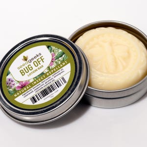 May include: A small, round tin container with a lid. The lid has a green and white label that reads "seedgeeks BUG OFF LOTION BAR NATURAL INSECT REPELLANT". The tin contains a round, white lotion bar with a butterfly design.